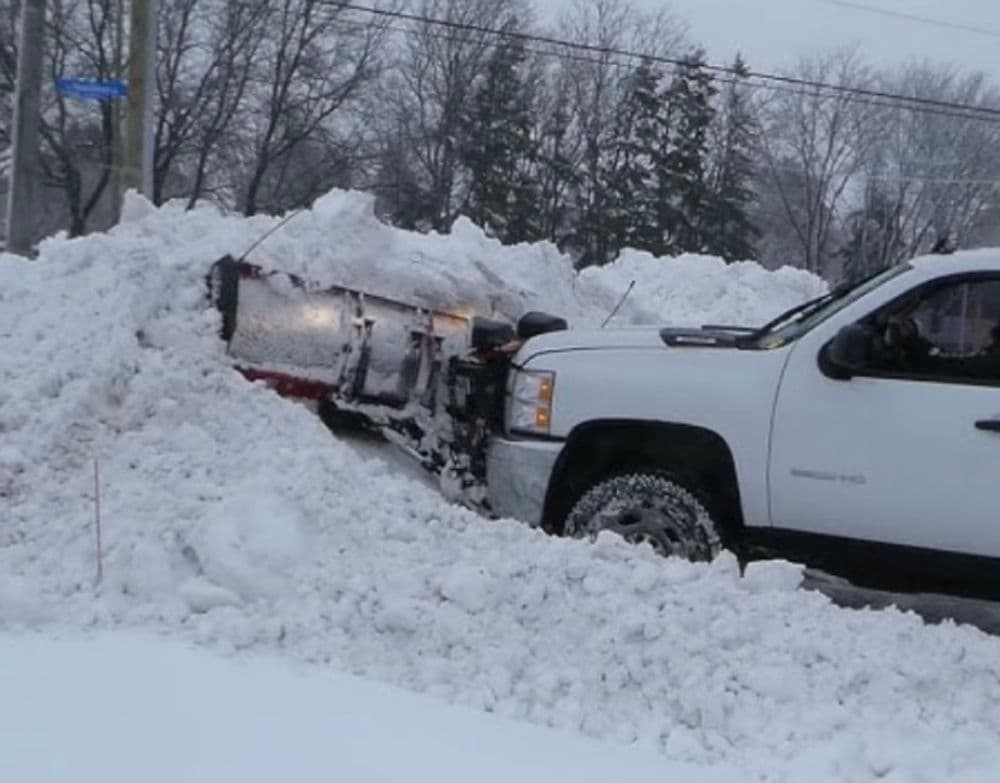 Snow plow truck clearing heavy snow from a residential street during winter storm.