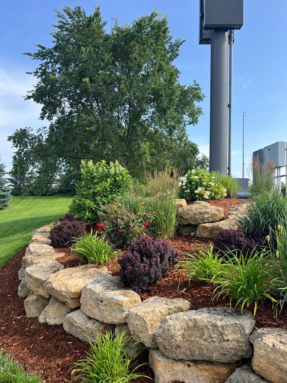 Vibrant landscaped garden with colorful flowers, lush greenery, and stone borders under a clear sky.