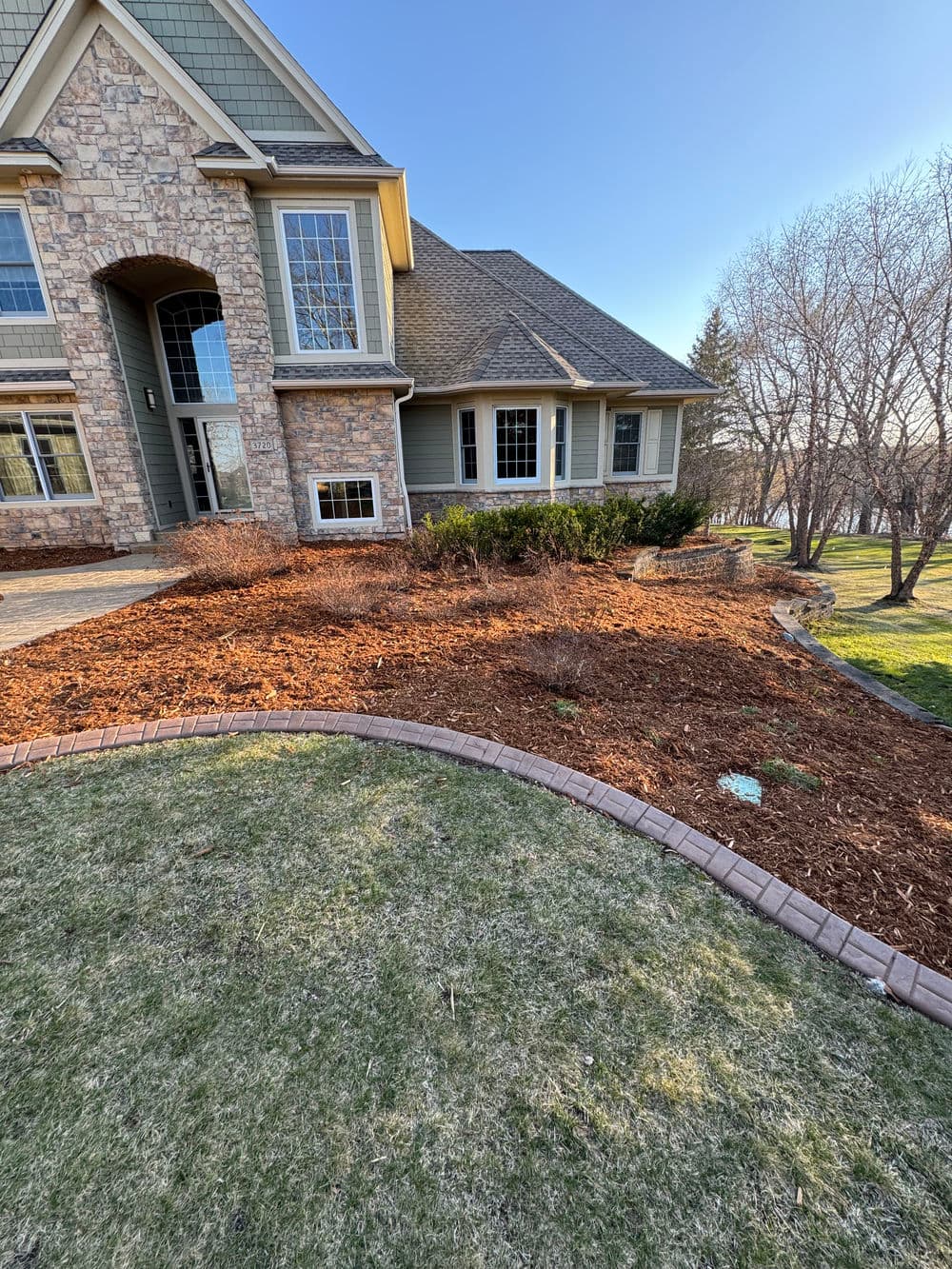 Landscape view of a home with stone exterior and fresh mulch in garden beds.