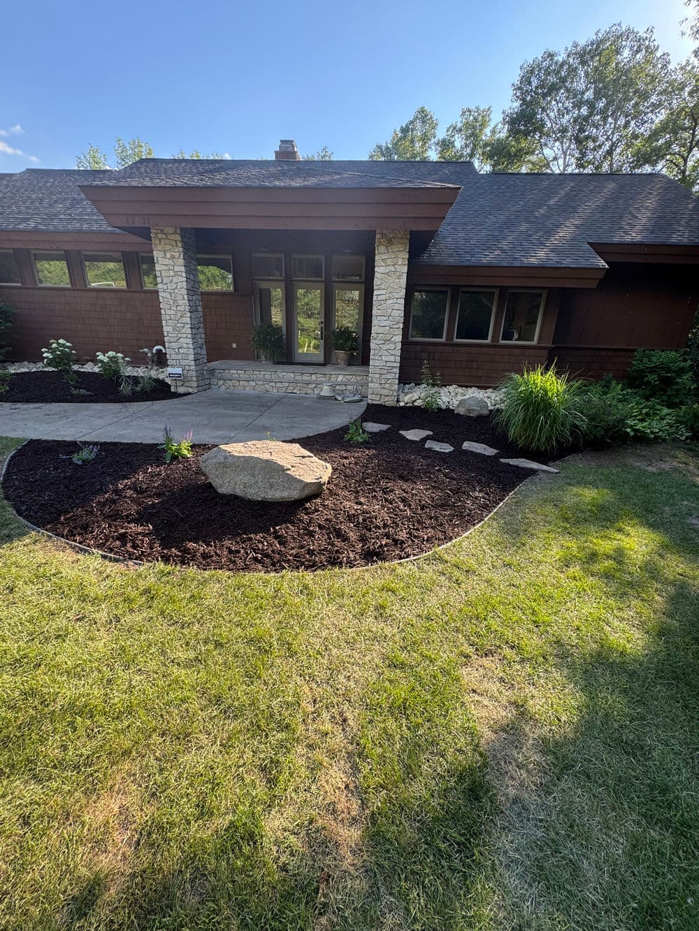 Modern home entrance with stone pathway, landscaping, and greenery under a clear blue sky.