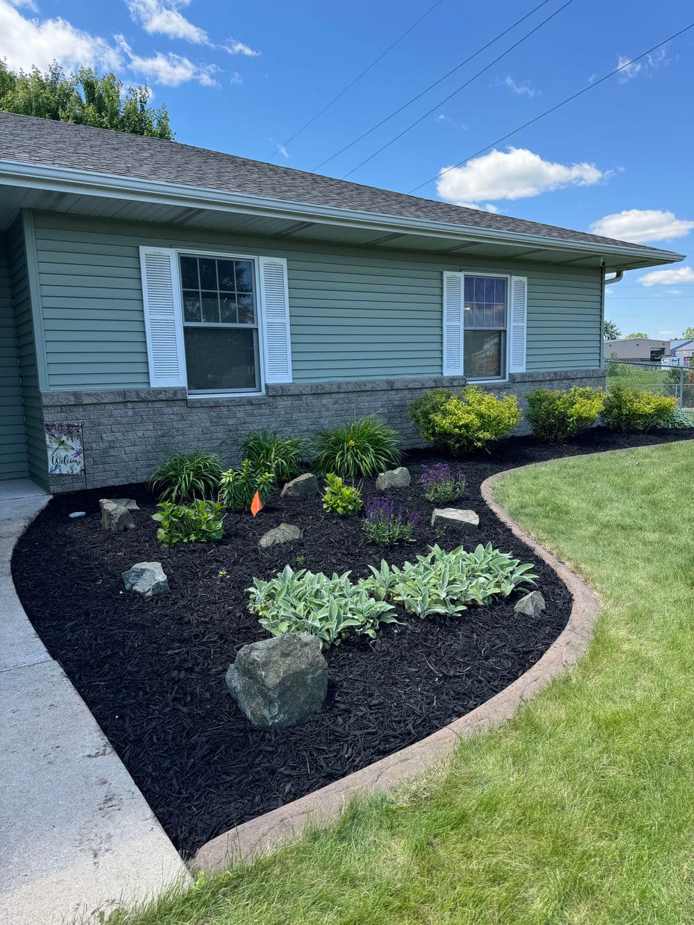 Charming front yard landscape with mulch, flowers, and shrubs beside a blue house.