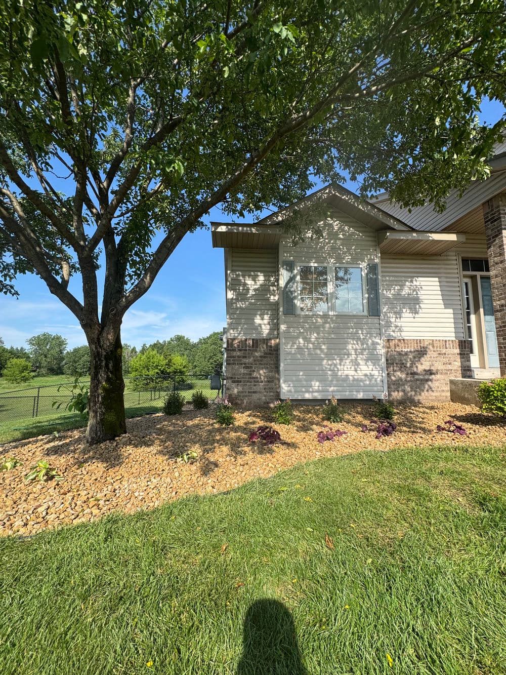 Single-story house exterior with landscaped garden, tree, and clear blue sky in background.