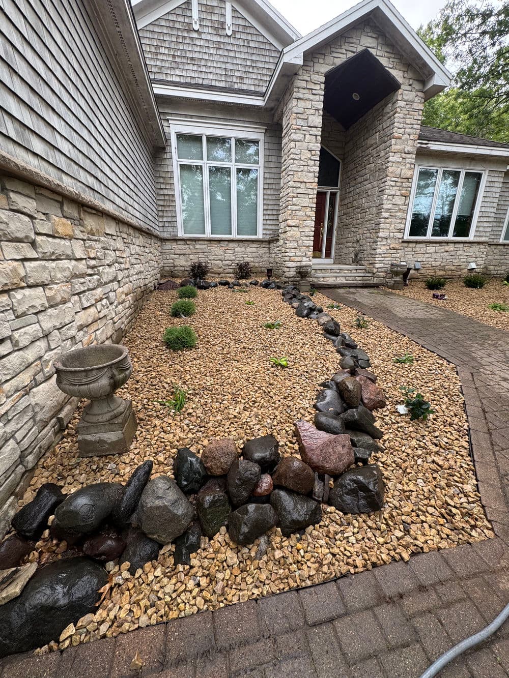 Front yard landscaping with decorative stones, gravel, and low shrubs leading to a home entrance.